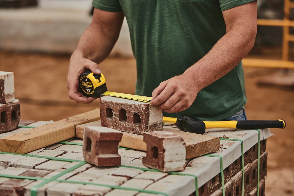 25 foot FATMAX classic tape measure being used by a person to measure length of a brick.