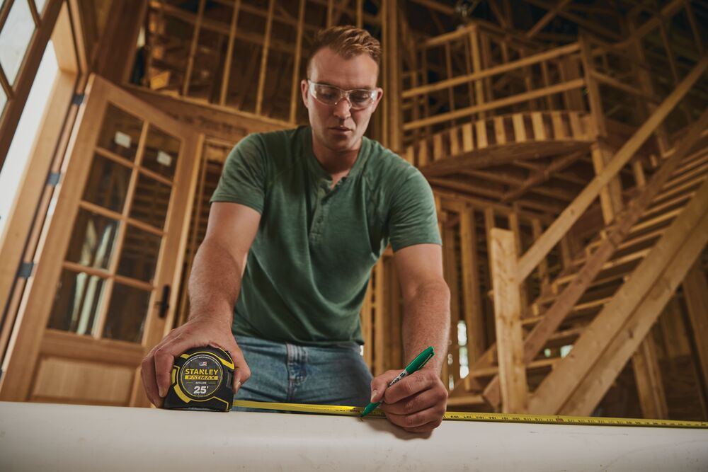 25 feet fatmax auto lock tape being used by a person to measure a wooden table.